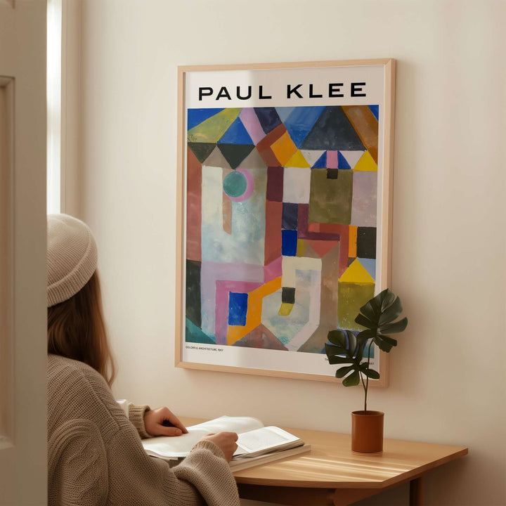 Person admiring a Paul Klee colorful architecture abstract geometric art print in a cozy interior setting.