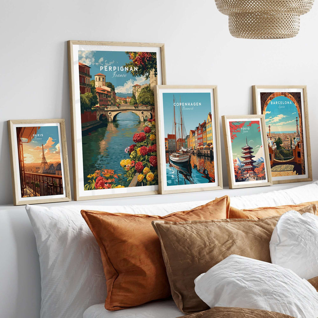 Framed Perpignan cityscape art print among other travel posters on a stylish couch, showcasing vibrant European landscapes.