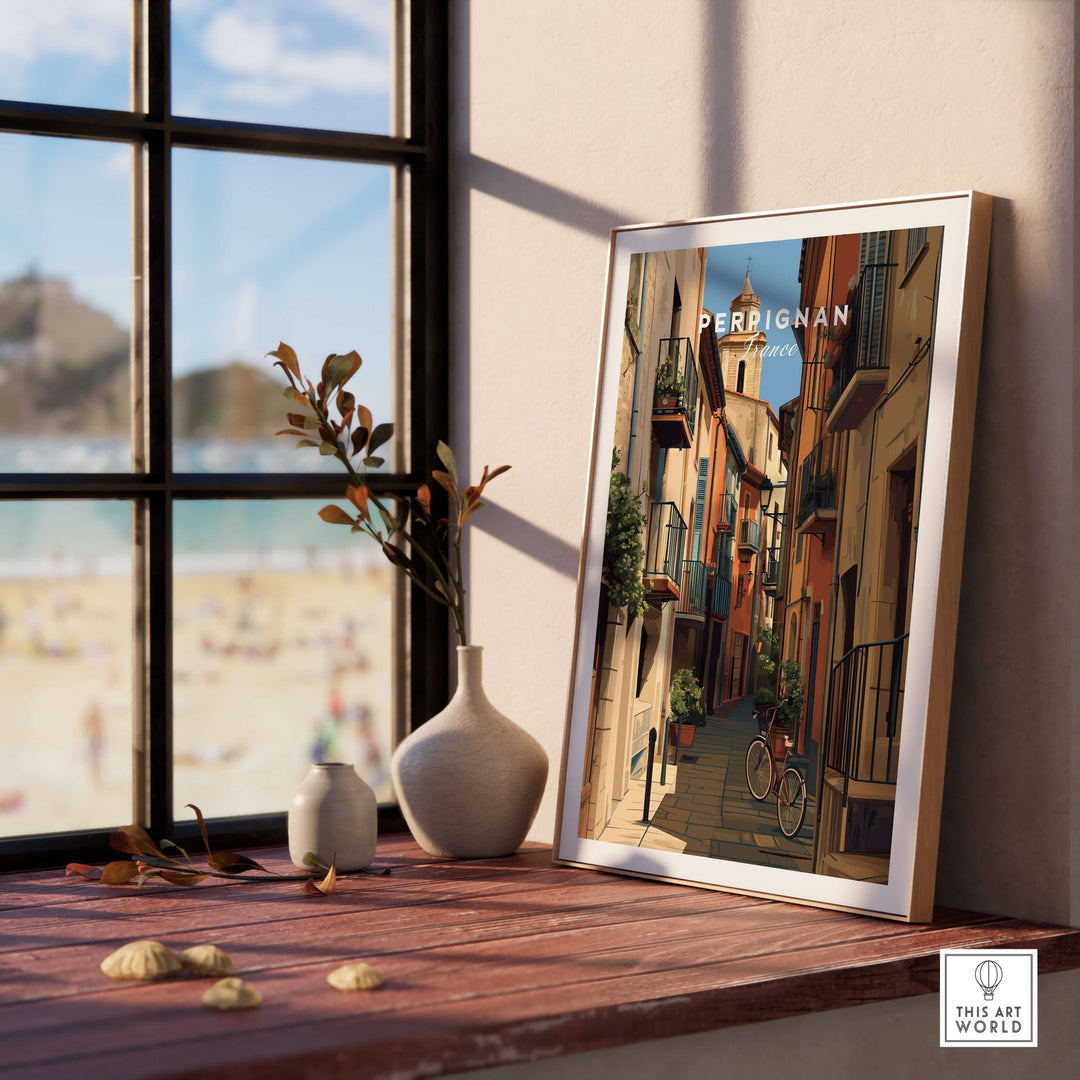 Perpignan poster art print displayed on a wooden table near a window, showcasing charming village life.