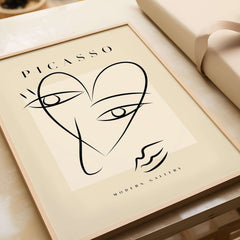 Picasso Line Art Abstract Heart Face Minimalist Modern Gallery Print Poster on beige backdrop in a wooden frame.