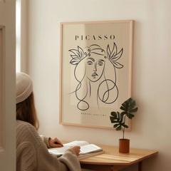 Picasso Line Art Woman Leaf Crown Modern Gallery Wall Art Poster framed on a wall with a person reading nearby.