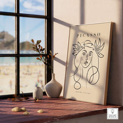 Picasso Line Art Woman Leaf Crown Modern Gallery Wall Art Poster displayed on a windowsill with beach view.