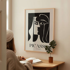 Picasso The Kiss 1979 Black White Abstract Profile Poster Art Print Wall Decor displayed on a wall near a person reading.
