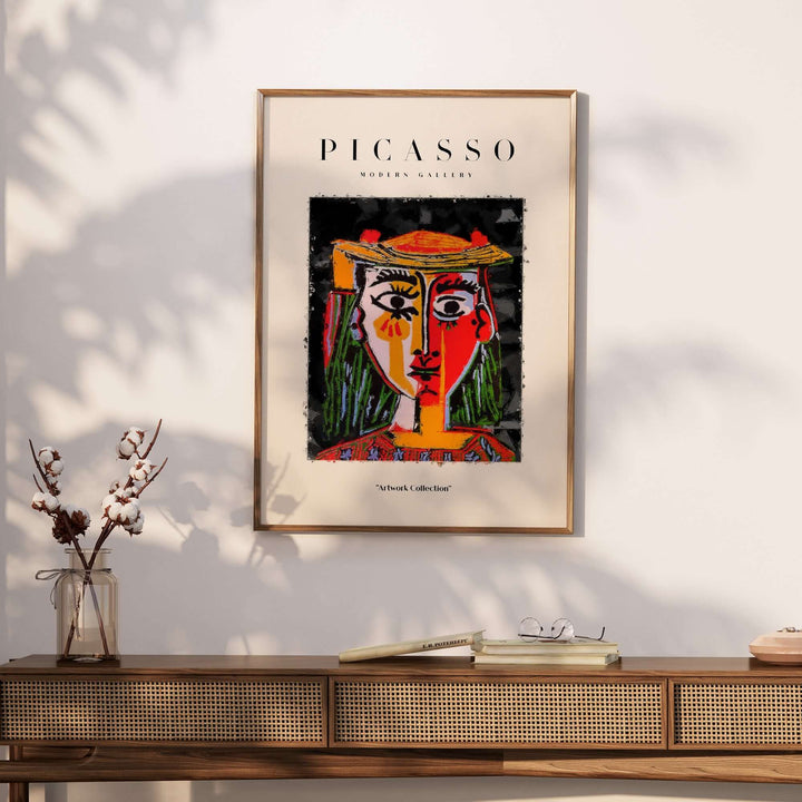 Colorful abstract portrait poster of a woman with a hat by Picasso in red, yellow, and green tones, framed on a wall.