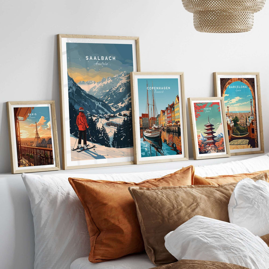 Saalbach travel poster alongside framed prints of Copenhagen and Barcelona, displayed on a cozy bed with velvet pillows.