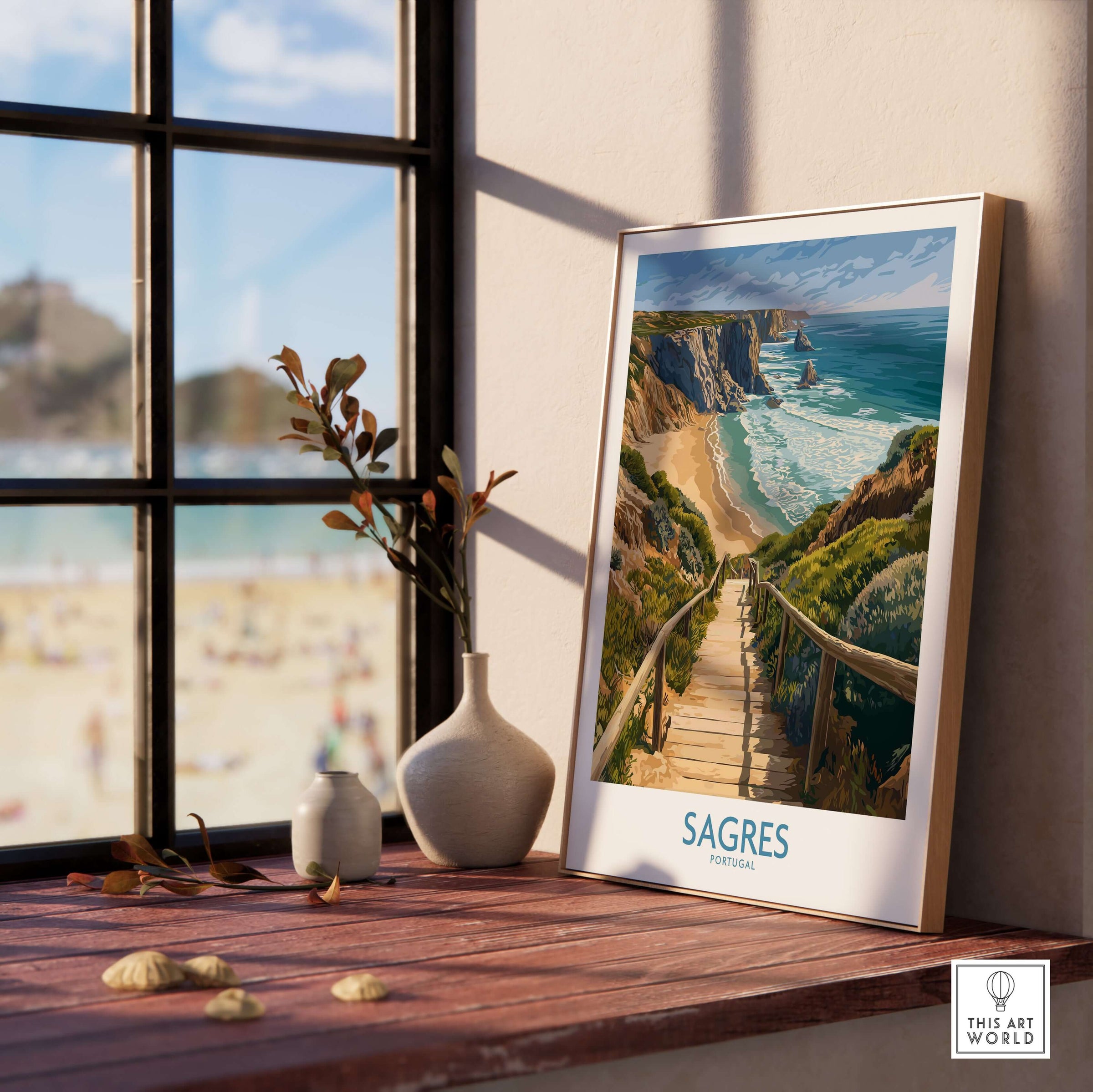 Sagres Poster Portugal Beach Art Print displayed on a wooden surface near a window, showcasing the Algarve's coast.
