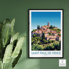 Saint Paul de Vence Travel Poster - French Riviera Wall Art - South of France Print displayed on a green wall with plants.
