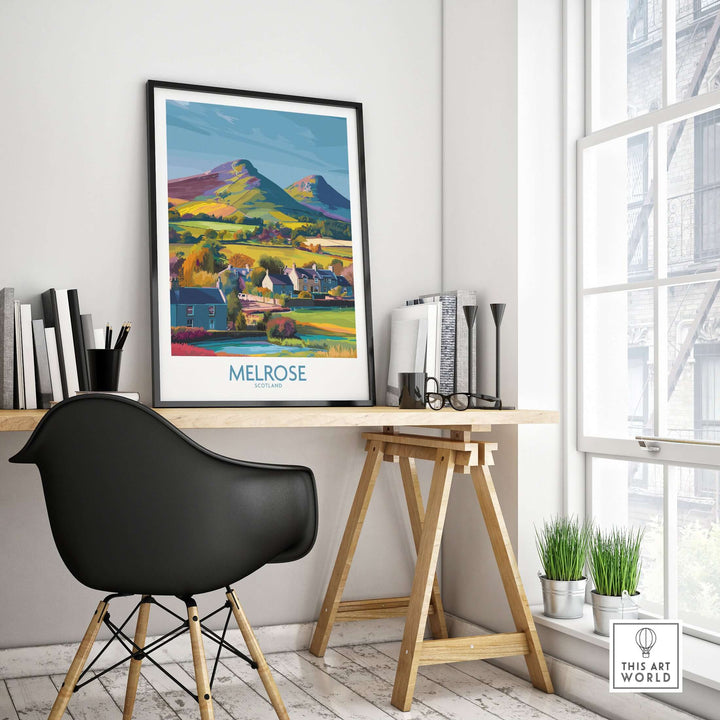 Colorful travel poster of Melrose Village and Eildon Hills in Scotland, displayed in a modern home office setting.