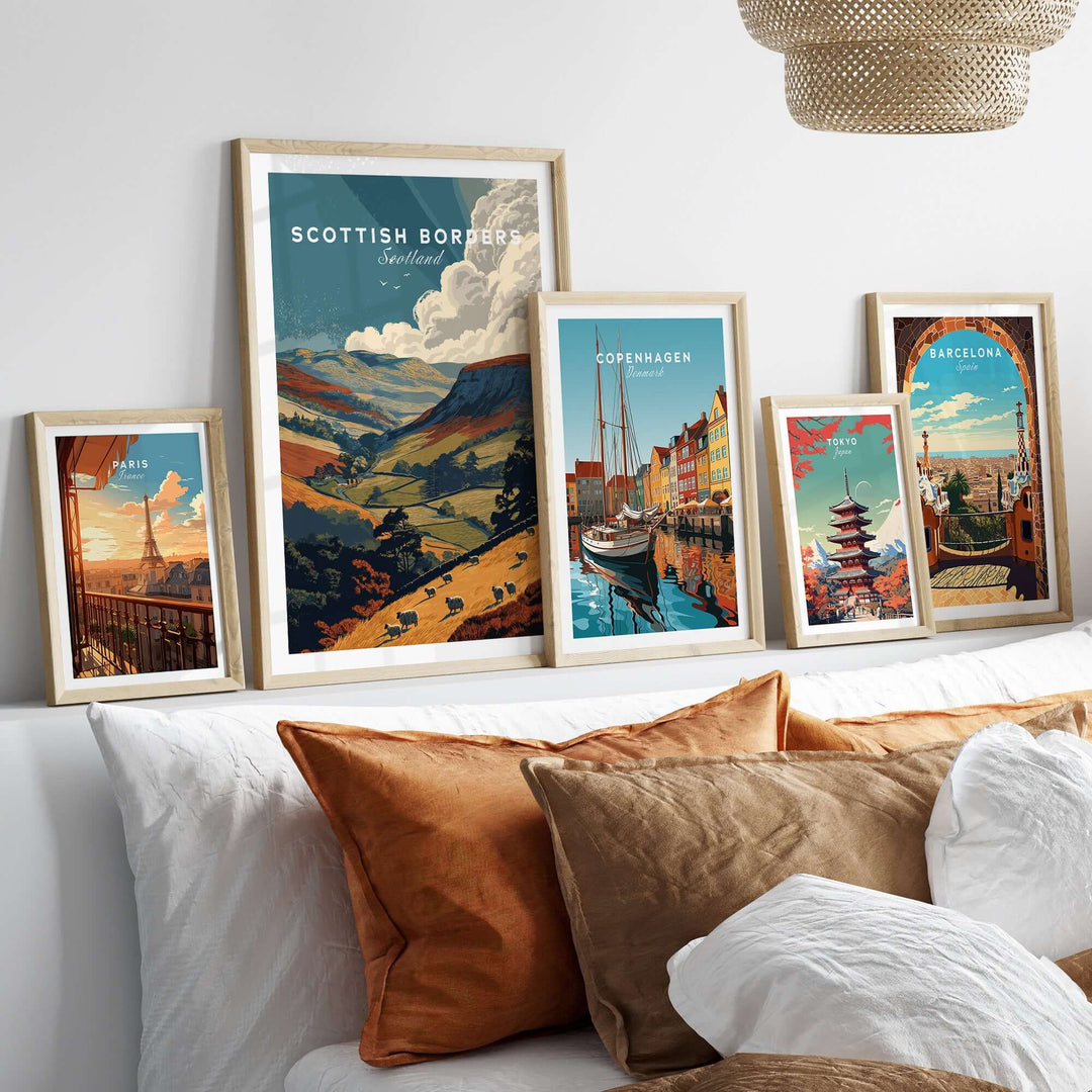 Framed travel posters of Scottish Borders, Copenhagen, and Barcelona on a bed with decorative pillows.