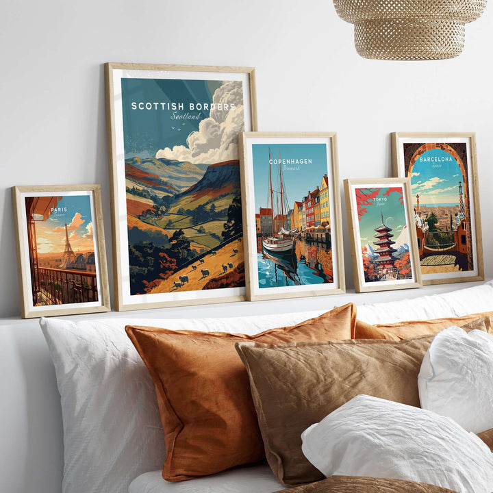 Framed travel posters of Scottish Borders, Copenhagen, and Barcelona on a bed with decorative pillows.