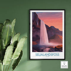 Seljalandsfoss Iceland Sunset Waterfall Art Print | Pink Sky Travel Poster framed on a green wall with leafy plants.