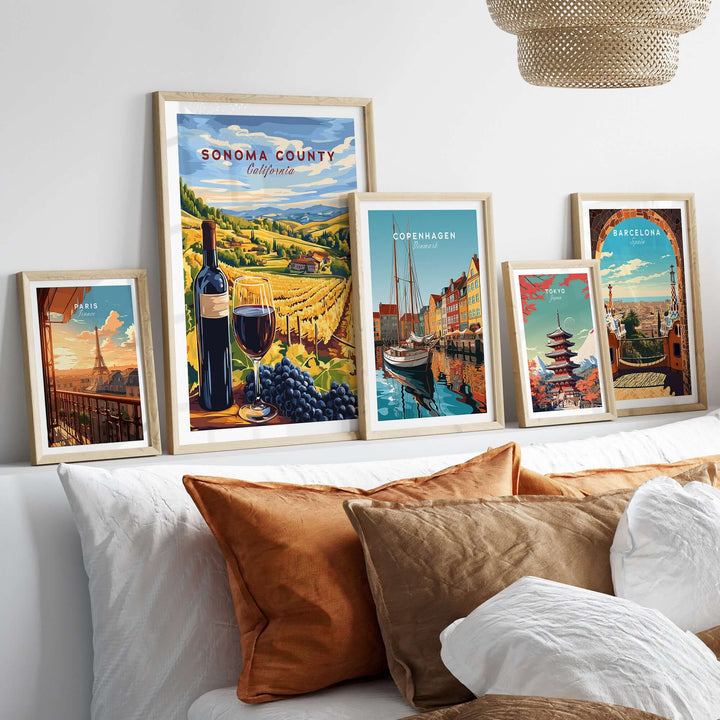 Framed Sonoma County wine poster with travel prints of Copenhagen and Barcelona above a cozy sofa with decorative cushions.