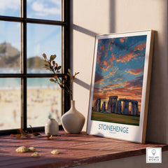 Stonehenge Poster - England Prehistoric Site Art Print - Orange Sky Wall Decor displayed on a wooden table next to a window.
