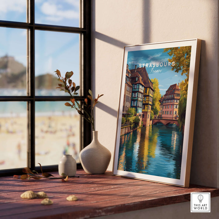 Strasbourg Print France Poster displayed on a wooden shelf near a window, showcasing scenic architecture and water.