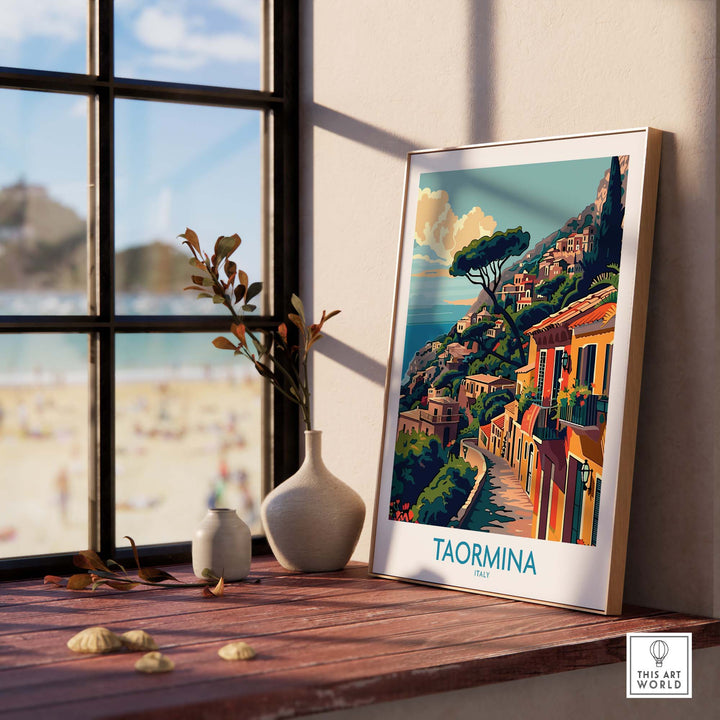 Taormina Travel Print displayed on a windowsill with a beach view in the background