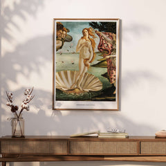 The Birth of Venus Art Print Sandro Botticelli Mythology Poster on a wall above a wooden table with decorative plants.