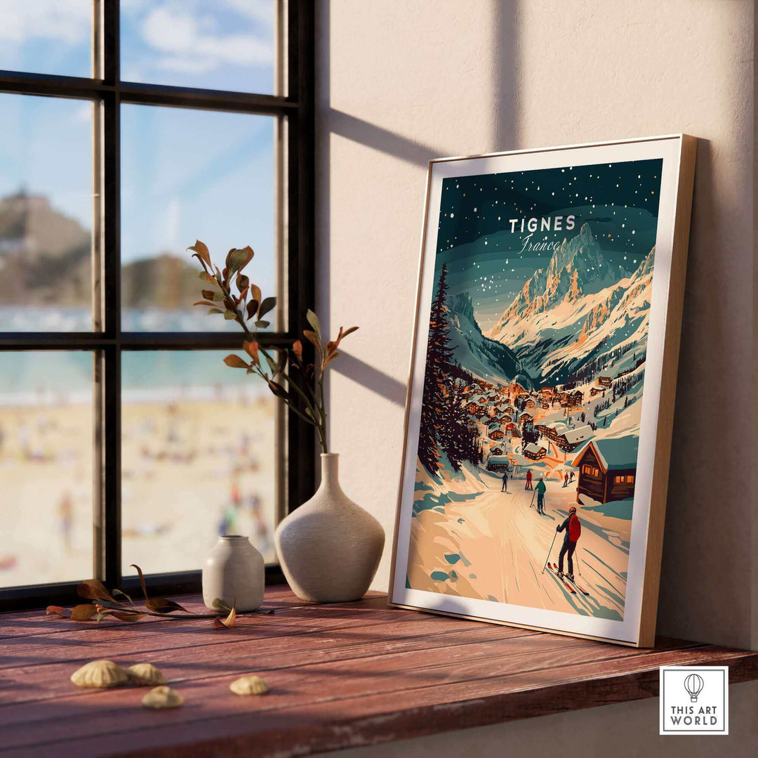 Scenic Tignes wall art ski print displayed on a sunlit windowsill, capturing a winter mountain landscape with skiers and a snowy village.