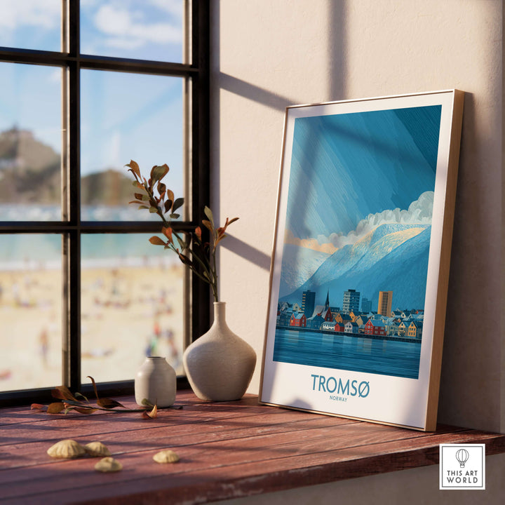 Tromsø Norway Art Print | Snowy Mountain City Poster displayed on a wooden shelf by a window with a beach view.