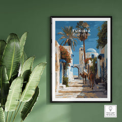 Tunisia Street Scene Print - Camels in the City Poster - Historic Town Wall Decor displayed on green wall with plants.