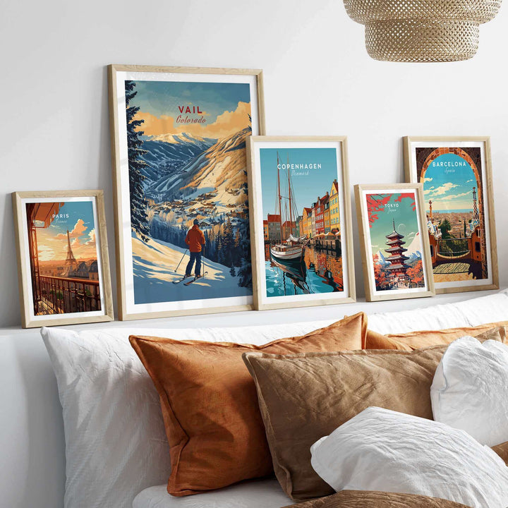 Collection of framed travel posters featuring Vail, Colorado skiing and cityscapes from Copenhagen and Barcelona displayed above a couch.