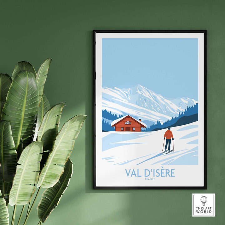 Val-d'Isère France art print with skier and mountain chalet, displayed against a green wall, indoor plant beside it.