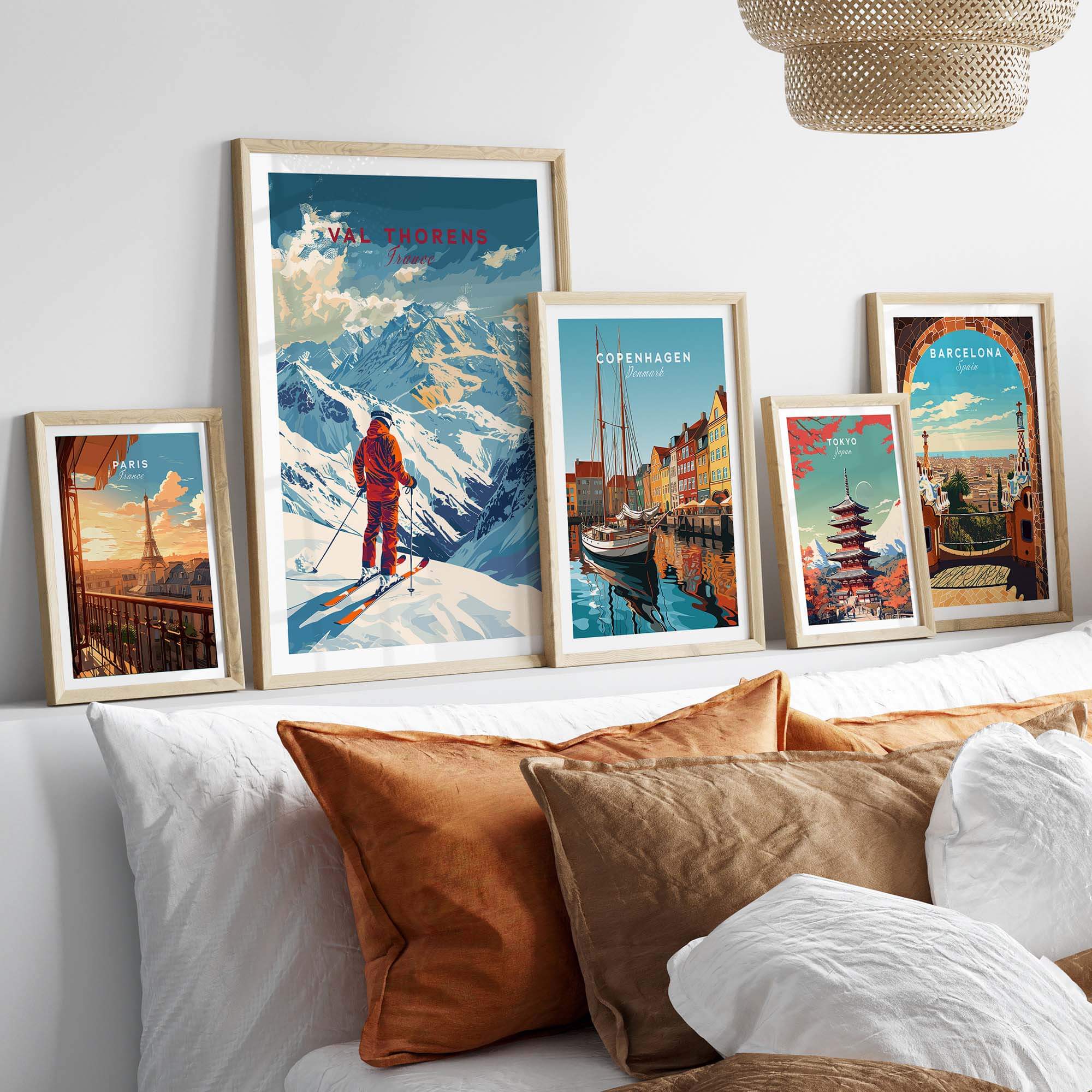 Framed Val Thorens ski poster alongside other vibrant city prints on a cozy bed with decorative pillows.