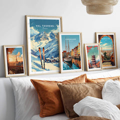 Val Thorens travel poster displayed among other city prints on a cozy sofa, showcasing beautiful ski slopes and vibrant scenery.