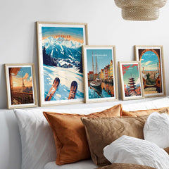 Framed ski prints of Verbier, Copenhagen, and Barcelona displayed on a bed with decorative pillows.