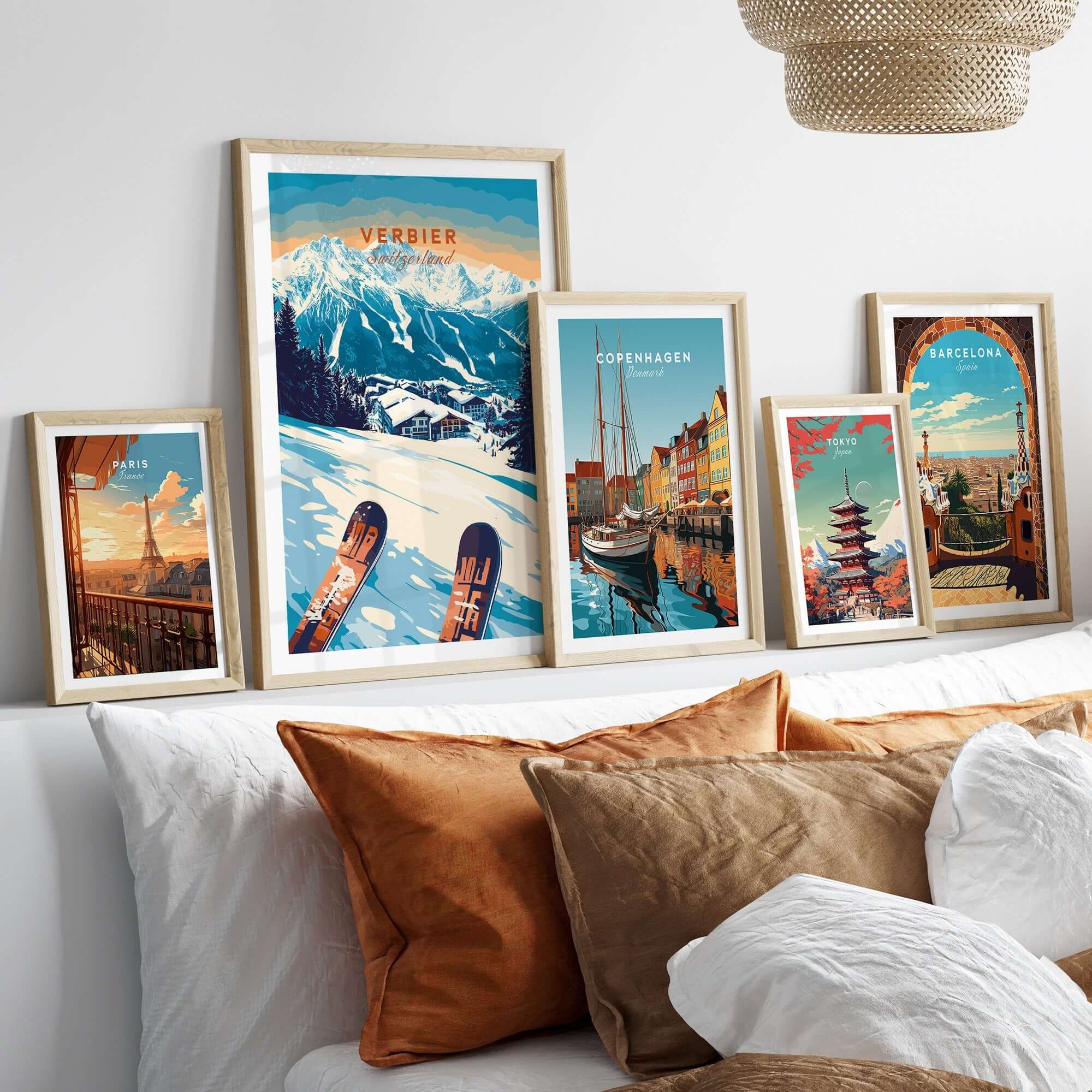 Framed ski prints of Verbier, Copenhagen, and Barcelona displayed on a bed with decorative pillows.