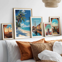 Zanzibar Print showcased among framed wall art on a bed, featuring vibrant tropical and cityscape designs.