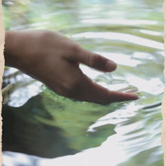 Person's hand gently touching rippling water surface in a serene outdoor setting.