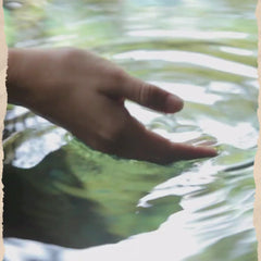 Close-up of a person's hand gently touching the surface of rippling water, creating mesmerizing circular waves.