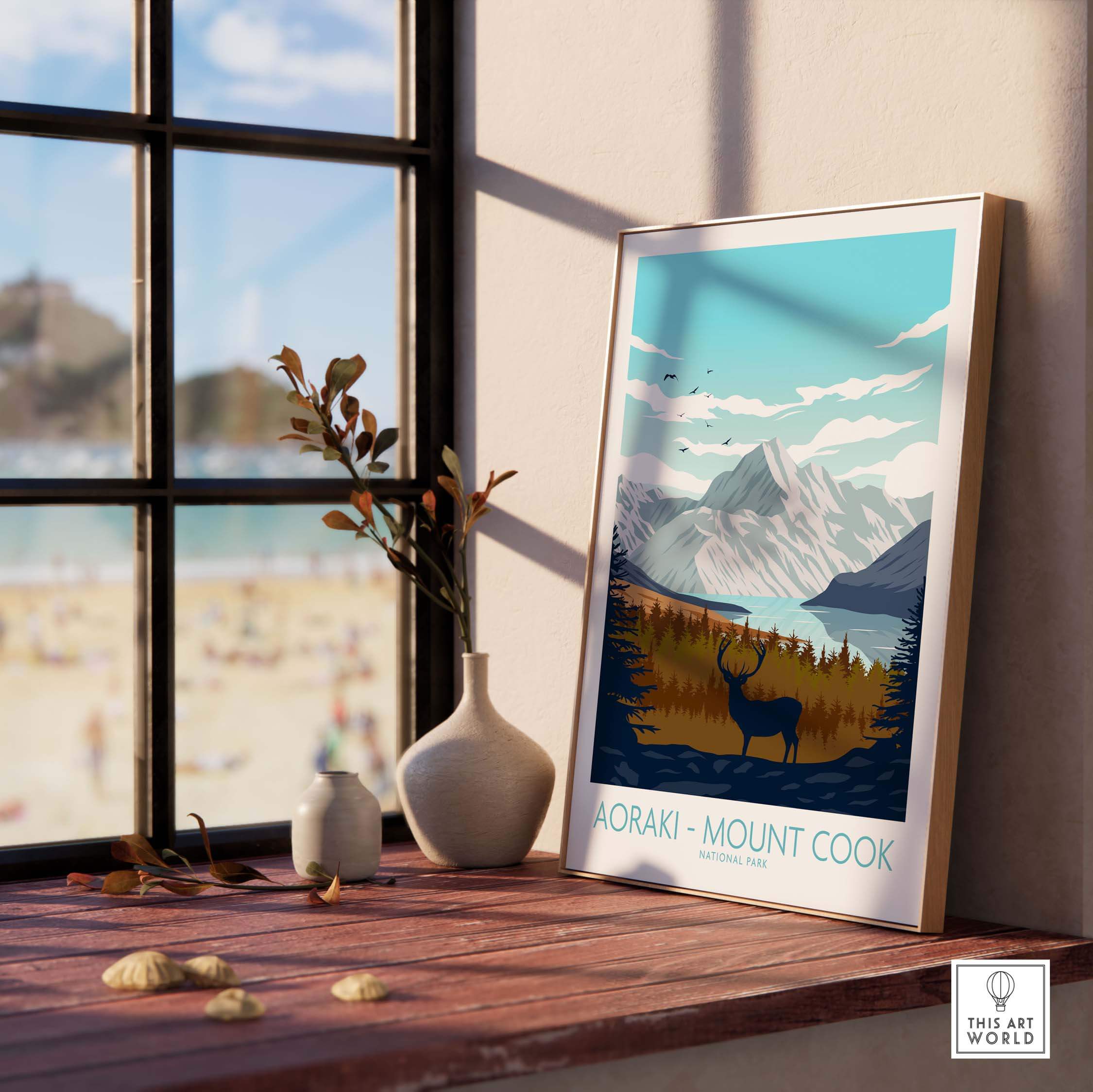 Aoraki Mount Cook poster displayed in a sunny interior, featuring mountains, a deer, and coastal scenery.