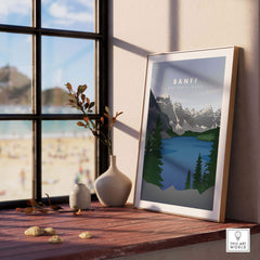 Framed Banff National Park art print featuring mountains and lake, set on a wooden table by a window.