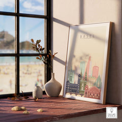 Basel City Skyline wall art print framed on a wooden table by a window, showcasing pastel-colored iconic architecture.