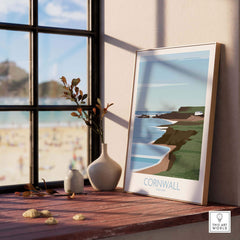 Cornwall Poster Print featuring coastal scenery, placed on a wooden table by a window, adding style to home decor.