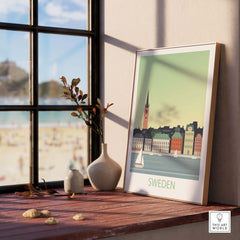 Sweden poster print displayed on a wooden table with a vase and beach view in the background, showcasing minimalist travel art.