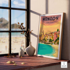 Menton France vintage print poster displayed on a wooden table by a sunlit window, featuring colorful coastal scenery.