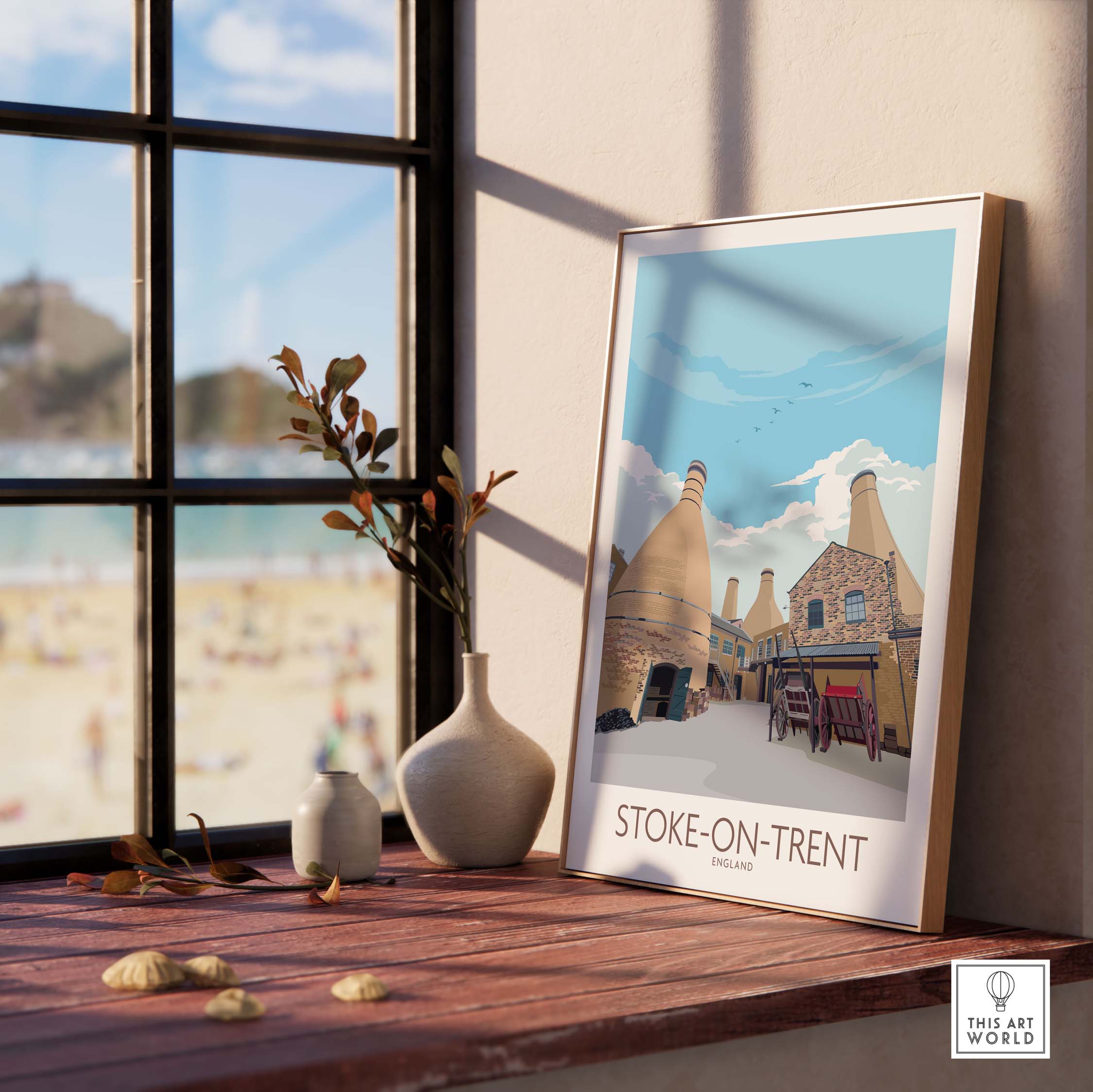 Framed Stoke on Trent print featuring vintage design, displayed on a wooden table by a window with beach view.