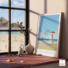 Framed The Hamptons wall art print on a wooden table by a window, showcasing a beach scene in a minimalist style.