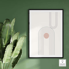 Abstract art print with geometric lines and soft colors on a green wall, surrounded by lush green plant leaves.