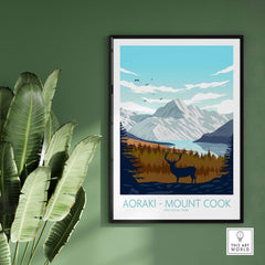 Aoraki Mount Cook poster featuring mountains, lake, and deer, displayed on a green wall with plants.