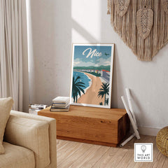 Nice France poster wall art print on a wooden table in a cozy living room with palm trees and beach view.