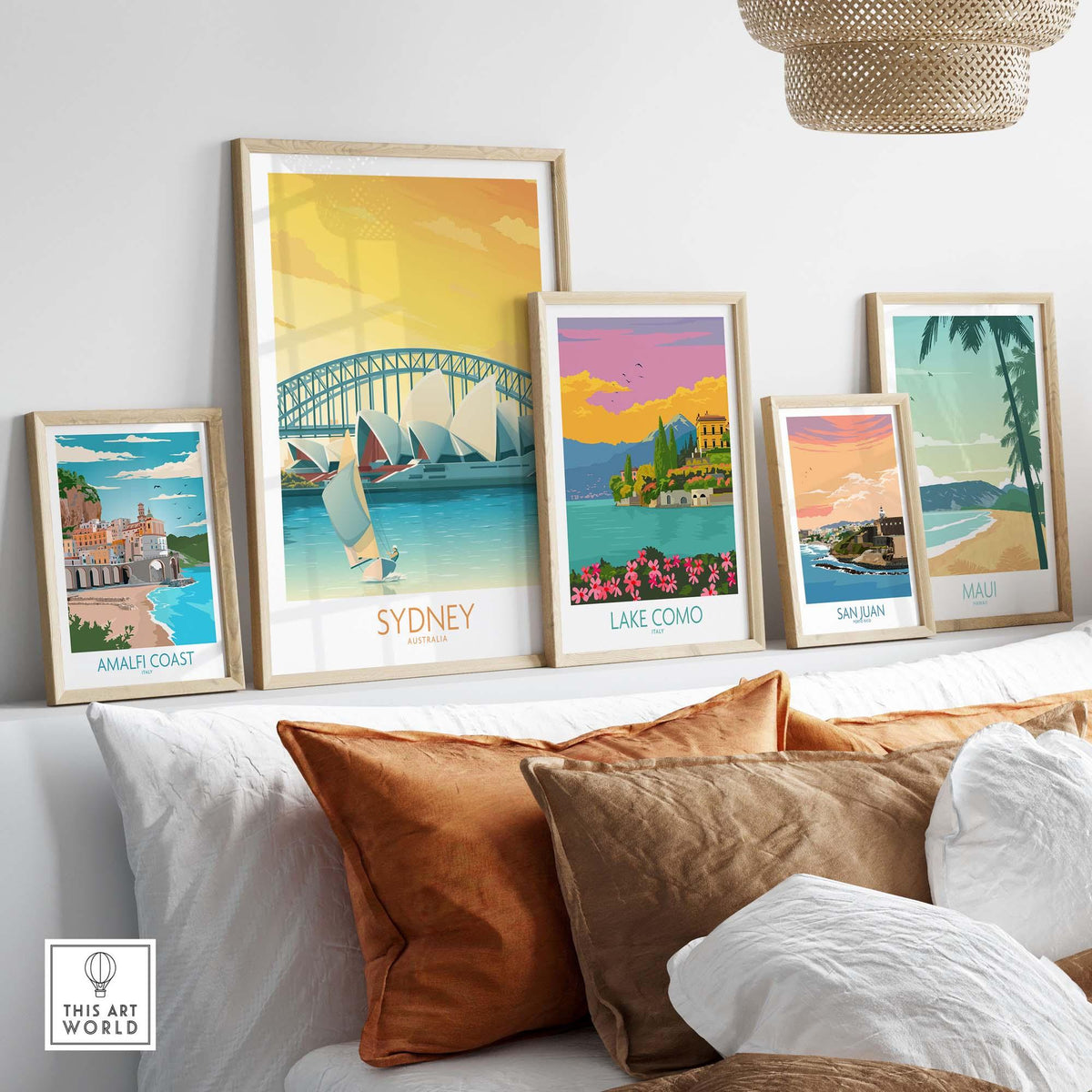 Framed travel posters including Sydney, Amalfi Coast, Lake Como, San Juan, and Maui displayed on a modern sofa.
