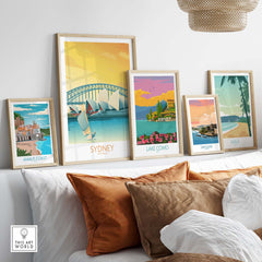 Framed travel posters including Sydney, Amalfi Coast, Lake Como, San Juan, and Maui displayed on a modern sofa.