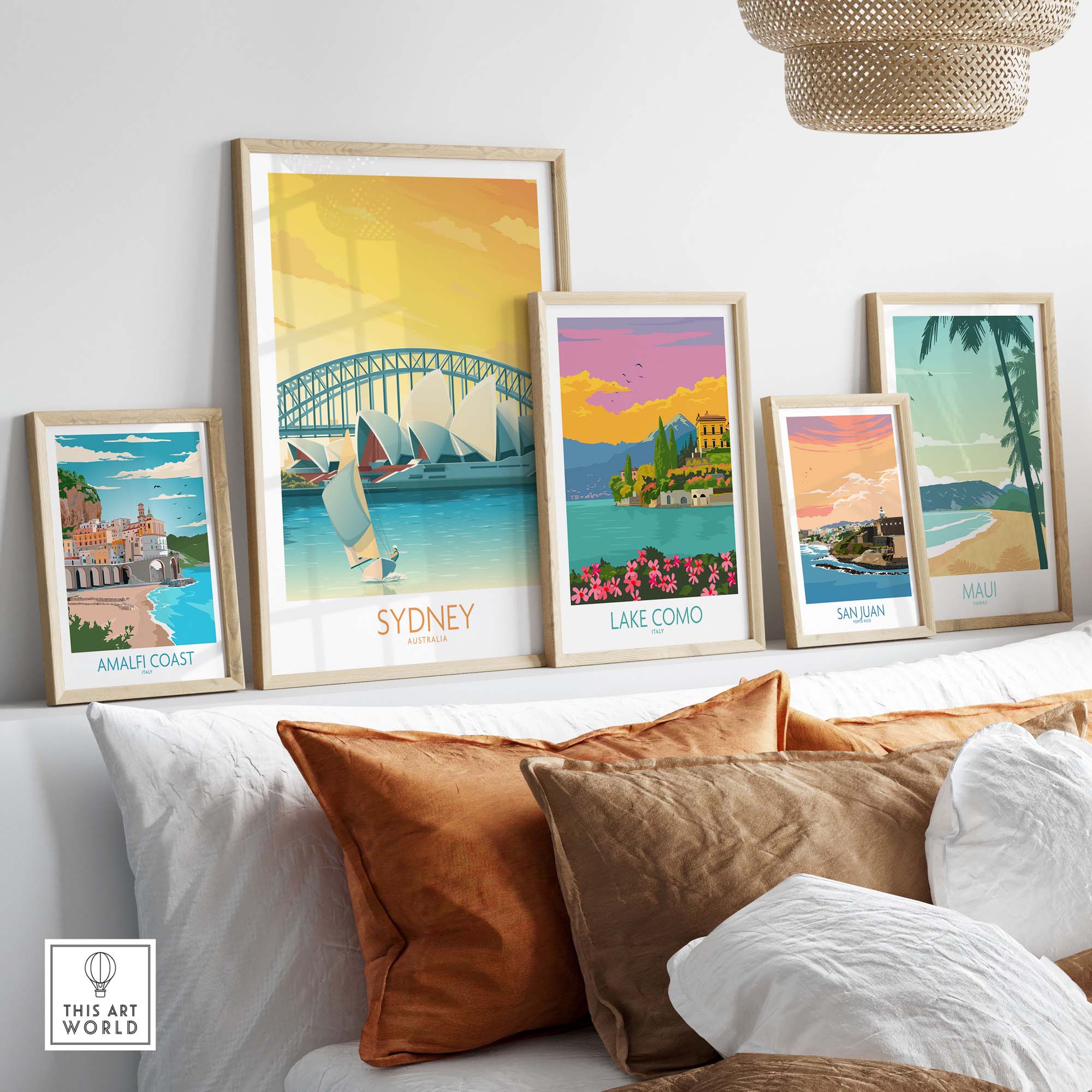 Framed travel posters including Sydney, Amalfi Coast, Lake Como, San Juan, and Maui displayed on a modern sofa.