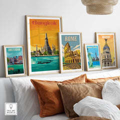 Framed vintage travel posters of Bangkok, Rome, Amsterdam, New York, and Madrid displayed on a wall above a sofa.