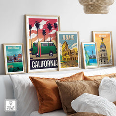 California travel poster wall art with framed prints of Amsterdam, Rome, New York, and Madrid on a couch.