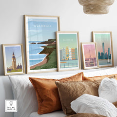 Stylish framed travel posters of Cornwall, London, Amsterdam, and Paris displayed above a sofa with decorative pillows.