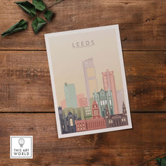 Leeds Print Skyline Wall Art featuring iconic buildings in warm pastel tones on a wooden surface.